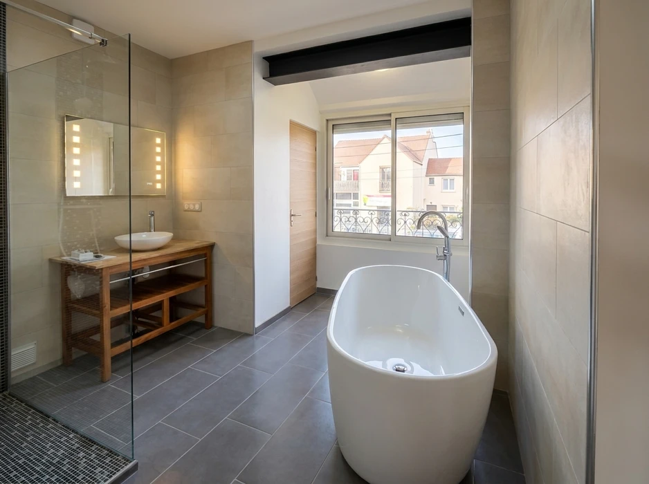 Salle de bain moderne et spacieuse avec baignoire îlot blanche autoportante, vasque à poser sur meuble console en teck, robinetterie chromée col de cygne, miroir LED encastré