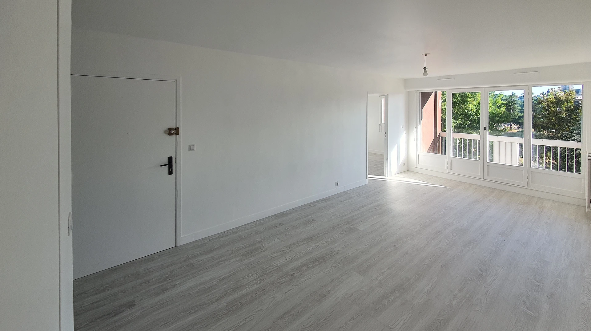Photographie réaliste d'une rénovation complète d'appartement montrant un espace de vie ouvert combinant cuisine équipée moderne et salon/séjour. La cuisine présente des façades laquées, un plan de travail contemporain, un îlot central ou un agencement optimisé, avec électroménagers encastrés et éclairage intégré. L'espace séjour adjacent bénéficie d'une décoration harmonieuse avec sol unifié et finitions épurées. Le tout doit transmettre l'idée d'une transformation cohérente et professionnelle d'un ensemble de pièces par un seul intervenant compétent, sans texte ni logo visible.